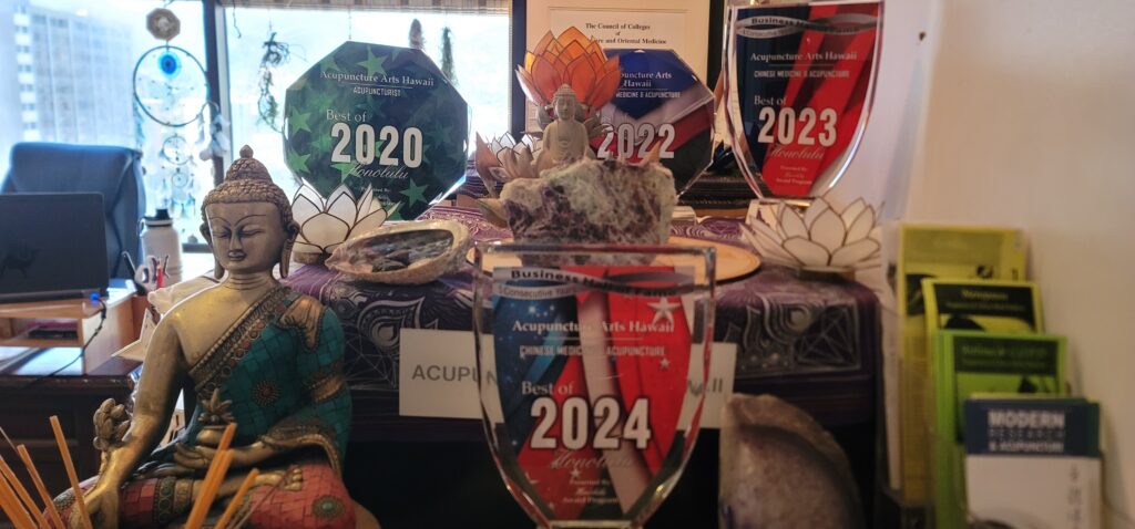 Awards display for Acupuncture Arts Hawaii featuring year plaques and a Buddha statue centerpiece.
